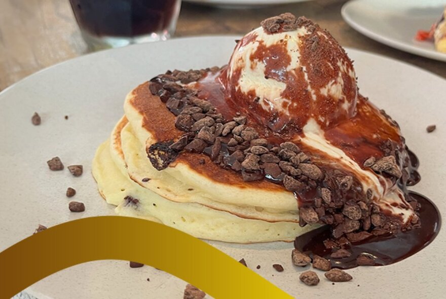 A plate of fluffy pancakes with ice-cream and chocolate over the top. 