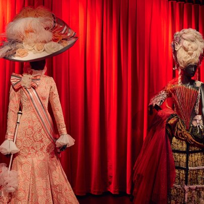 Two theatrical costumes on display in front of a red curtain, featured in the ENCORE! exhibition at the Australian Museum of Performing Arts.
