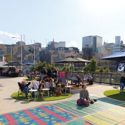 People lgathered on the Fed Square rooftop with yoga mats and shade umbrellas.