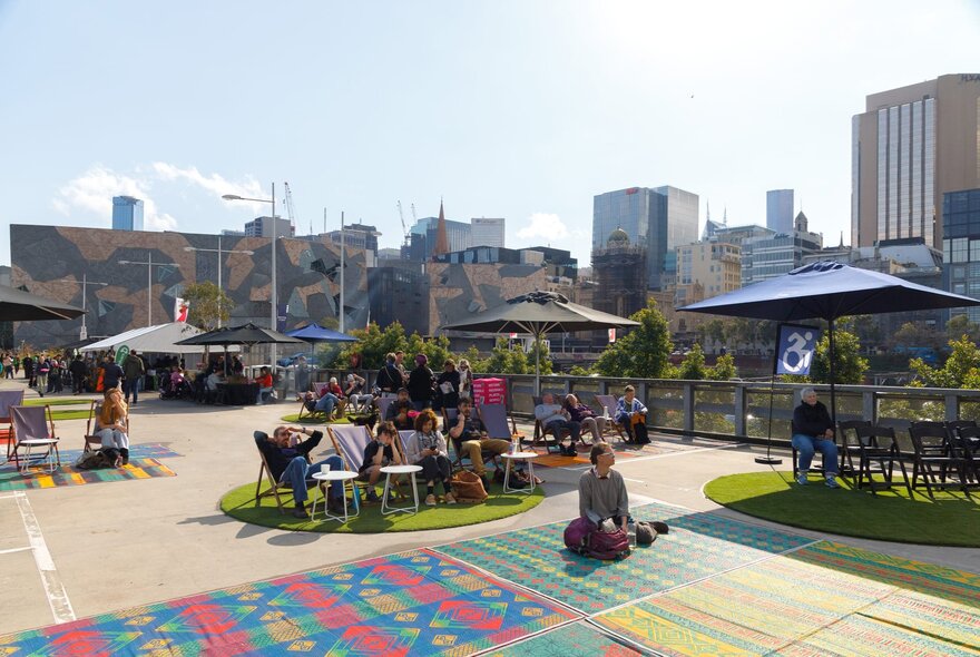 People lgathered on the Fed Square rooftop with yoga mats and shade umbrellas.
