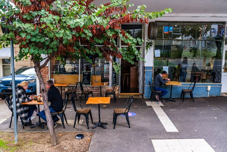 The exterior of Rolld169 cafe in Kensington, with people eating at tables on the footpath, and a green leafy tree in the foreground.