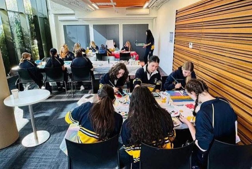 Young adults inside a studio space, creating artworks, seated around two tables.
