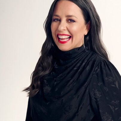 Media presenter Myf Warhurst, a smiling woman with long dark hair and red lipstick wearing a black long sleeved top.