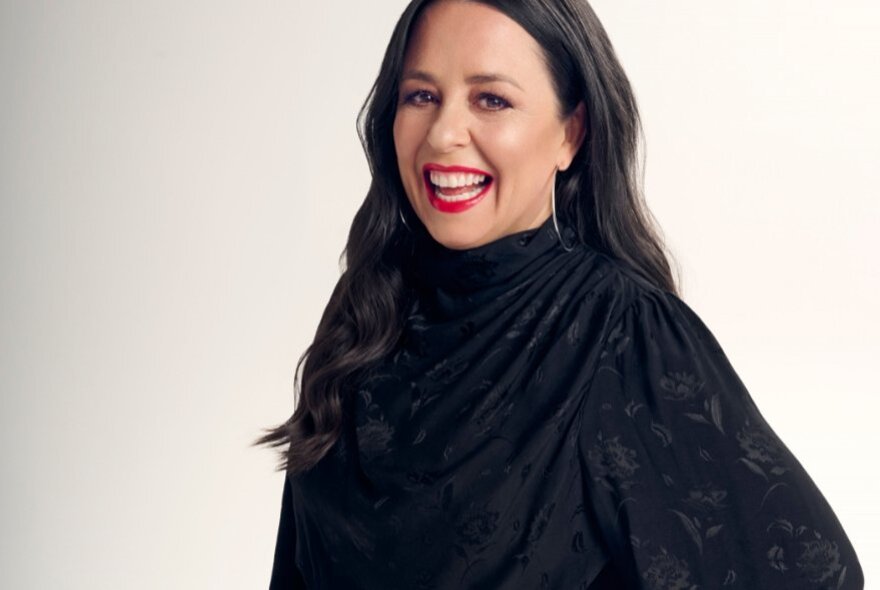 Media presenter Myf Warhurst, a smiling woman with long dark hair and red lipstick wearing a black long sleeved top.