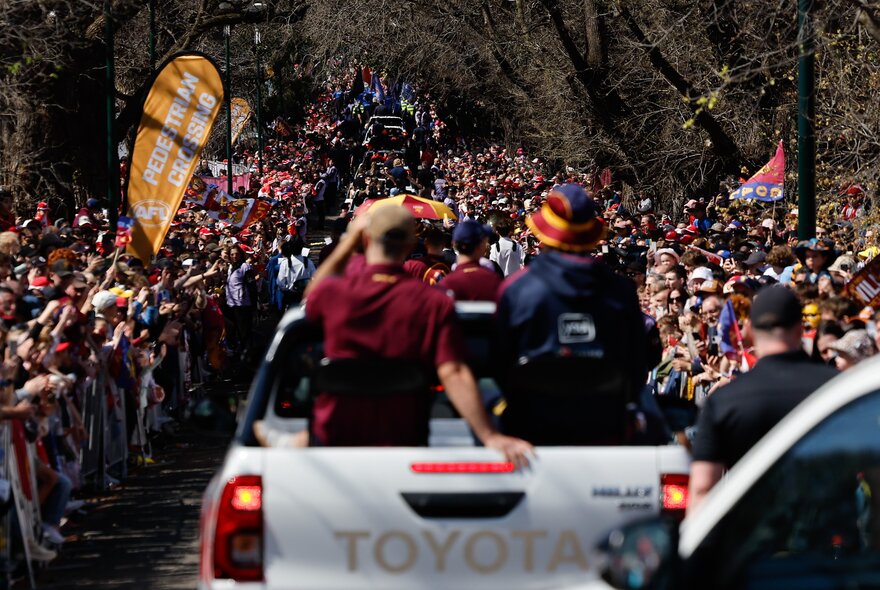 The Grand Final Parade motorcade with players in open air vehicles, with large crowds of footy fans lining the road on either side.