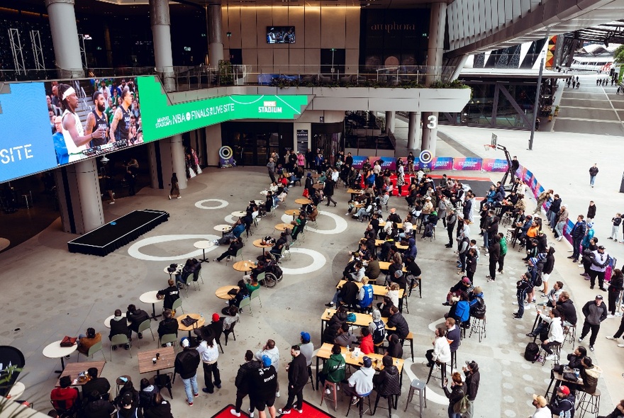Marvel Stadium's free live site for the 2025 NBA Finals, with a huge TV screen and tables and chairs in the forecourt of Marvel Stadium.