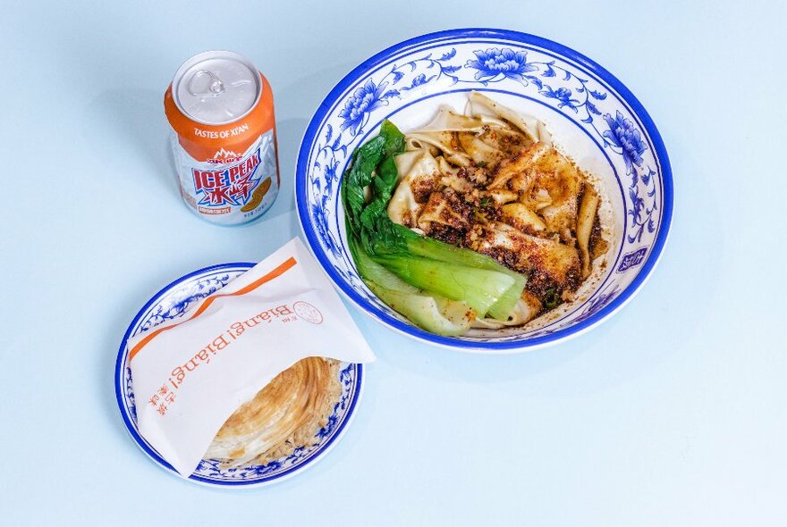 Bowl of Chinese noodles and vegetable, a drink and a burger.