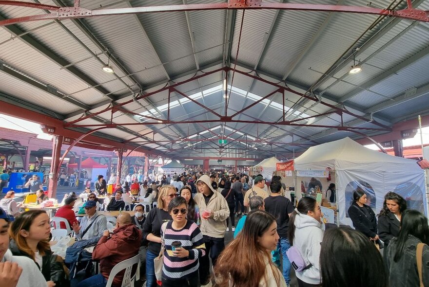 A crowd of people strolling past stalls at one of the undercover market sheds at Queen Victoria Market.