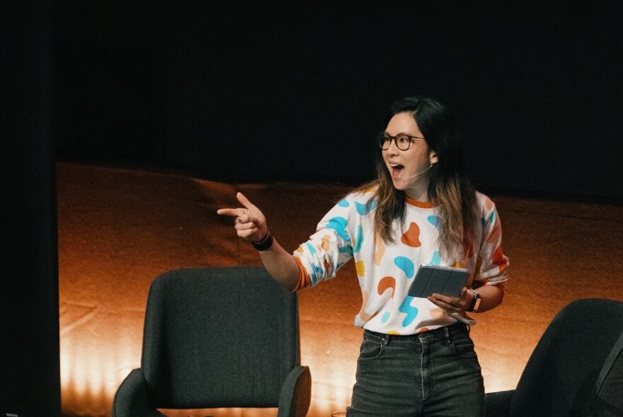 A presenter standing on a stage, holding a device, gesticulating.