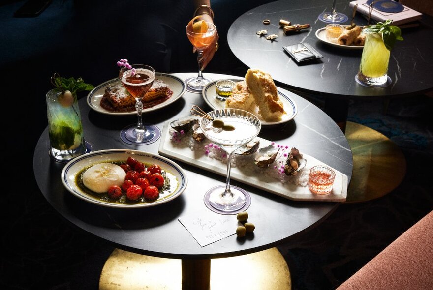 Plates of finger food and cocktails on small tables inside a nightclub.