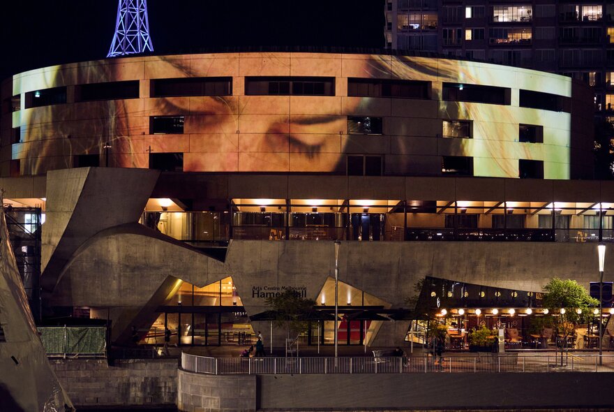 Hamer Hall building facade in Melbourne at night, with a large-scale projection of a person's face and eyes on the exterior.