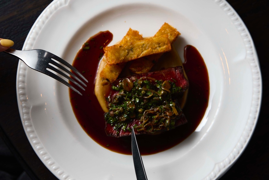 Knife and fork raised above a plating of meat and gravy on a white dish.