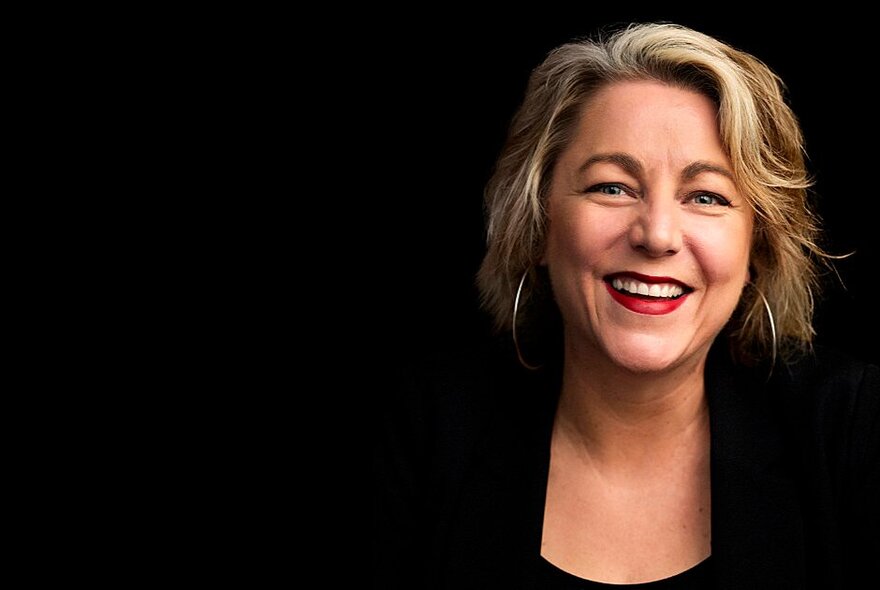 Presenter Nelly Thomas, smiling with streaked blonde hair and red lipstick.