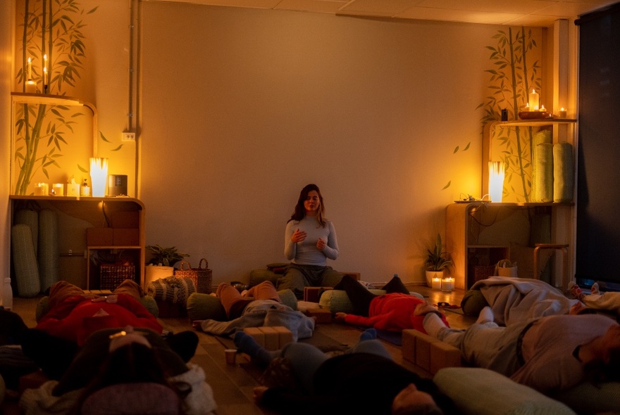 People attending a quiet yoga class, lying on mats in candlelight in a soothing space.