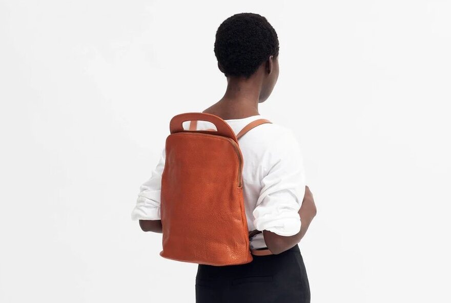 a woman is wearing a brown leather backpack