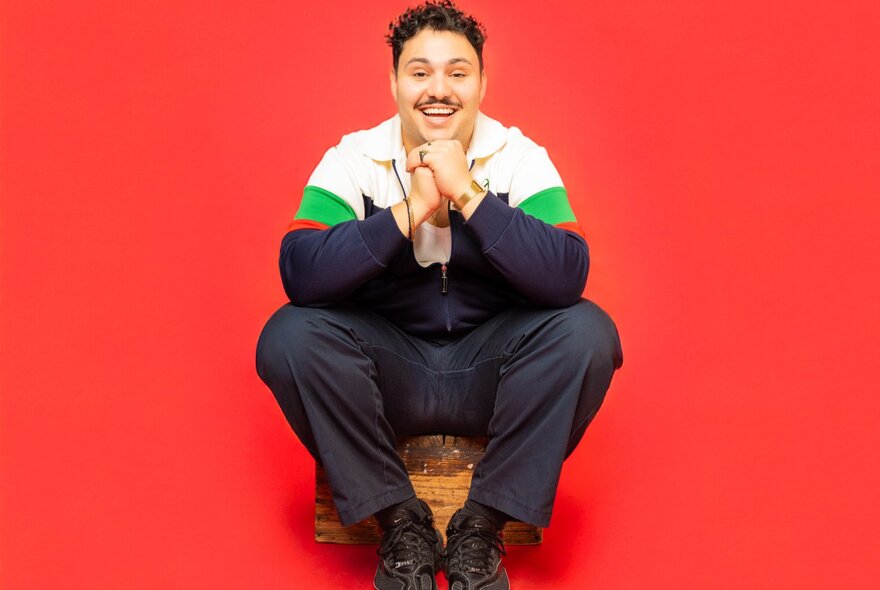 A person sitting in front of a red background, hands clasped together under their chin.