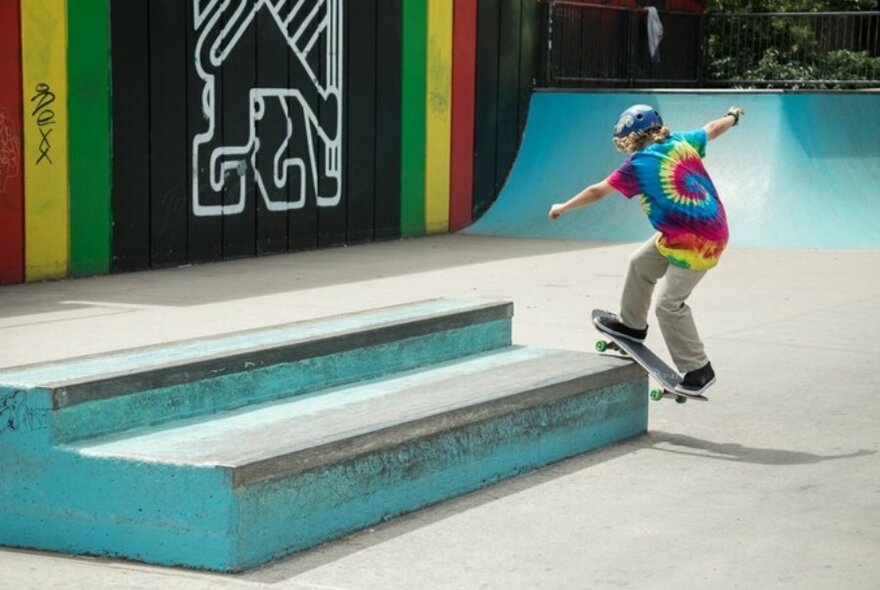 A boy in a tie-dye shirt skating at a public skatepark