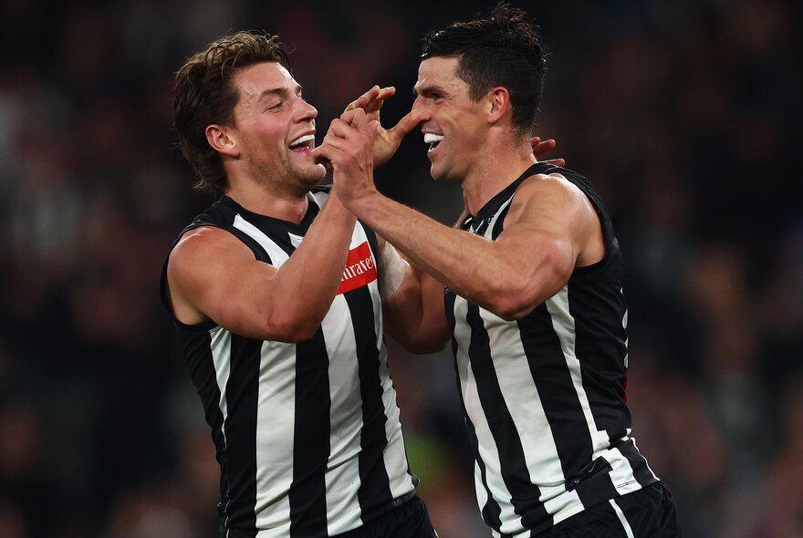 Two AFL Collingwood players high-fiving each other on the football field during a game.