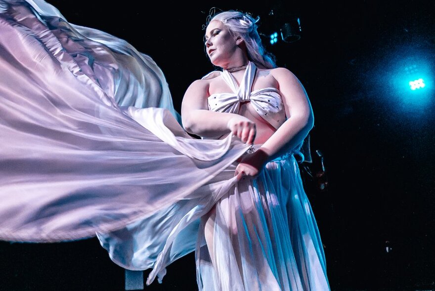 A majestic woman in a white flowing gown which is being blown by an air machine. 