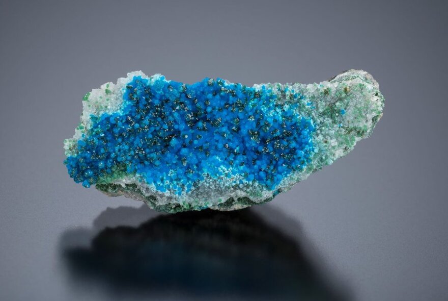 A blue and teal irregular-shaped crystal, resting on a dark surface.