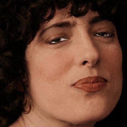 Close up of the face of comedian and actor Hannah Camilleri, she has slightly pursed lips and brown curly hair framing her face and the image appears to be hand coloured.