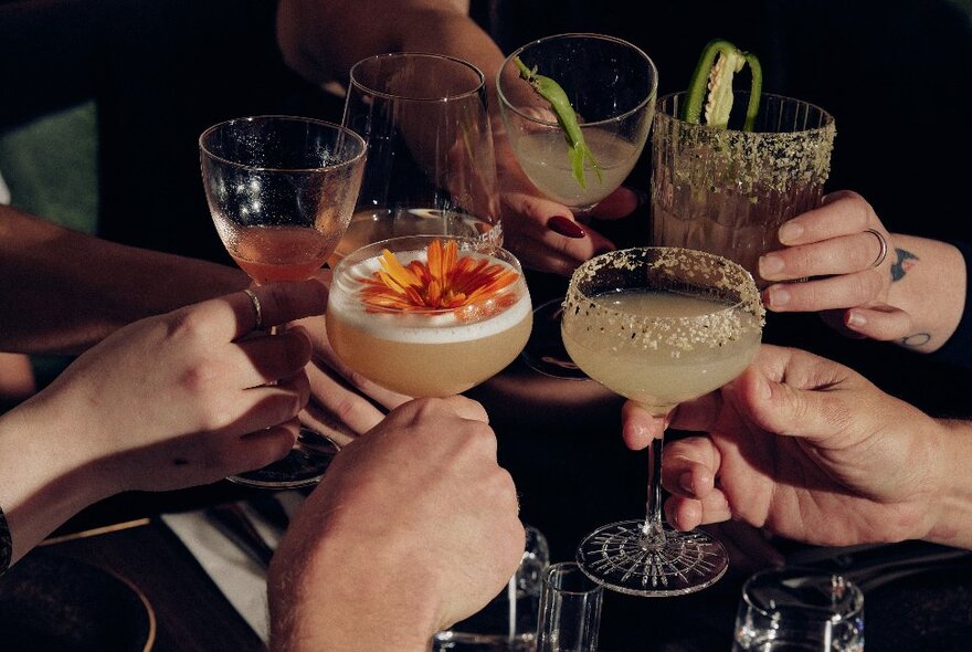 Hands clinking drinks glasses over a table.