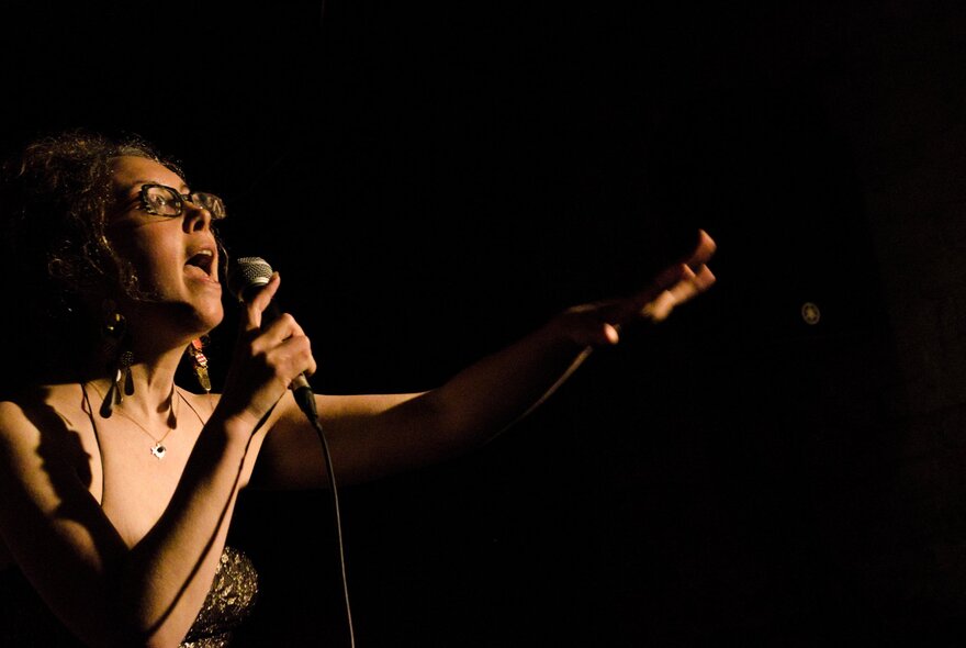 Singer holding a microphone, her arm outstretched.