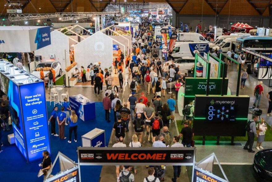 Overhead view of stalls at an expo in a large exhibition venue, with people walking around looking at the displays.