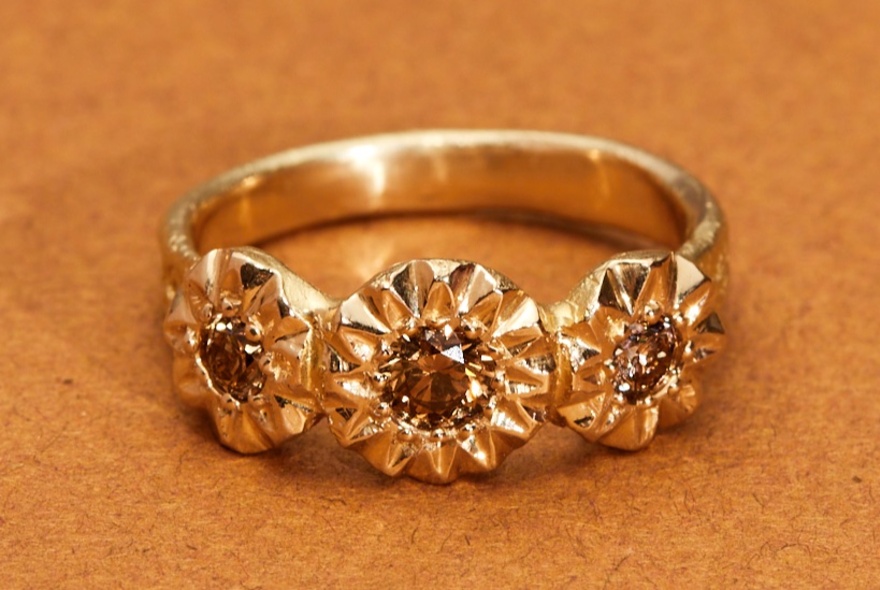 A gold ring with three stones set at the centre of flowers. 