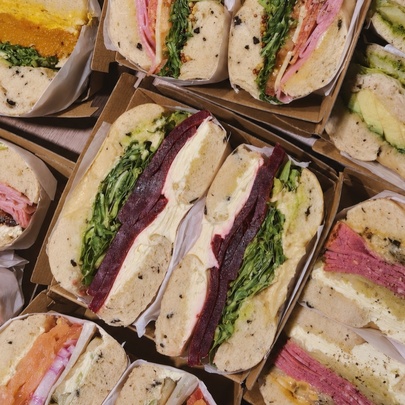 Several boxes filled with cut bagel sandwiches packed with fillings like greens, meats, and spreads.