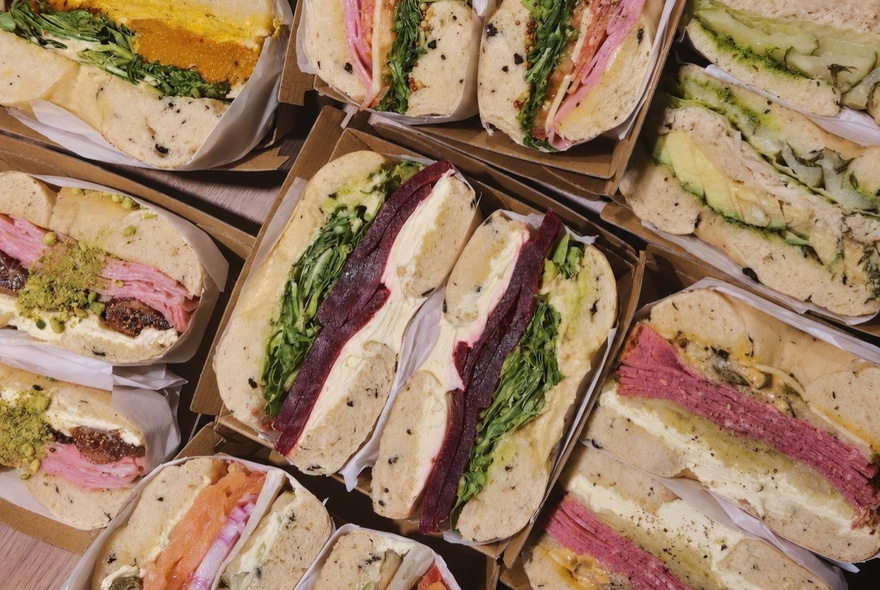 Several boxes filled with cut bagel sandwiches packed with fillings like greens, meats, and spreads.