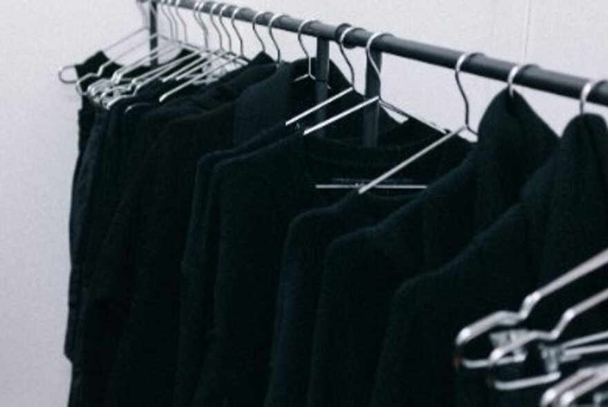 A rack of all-black clothes hanging on metal hangers.