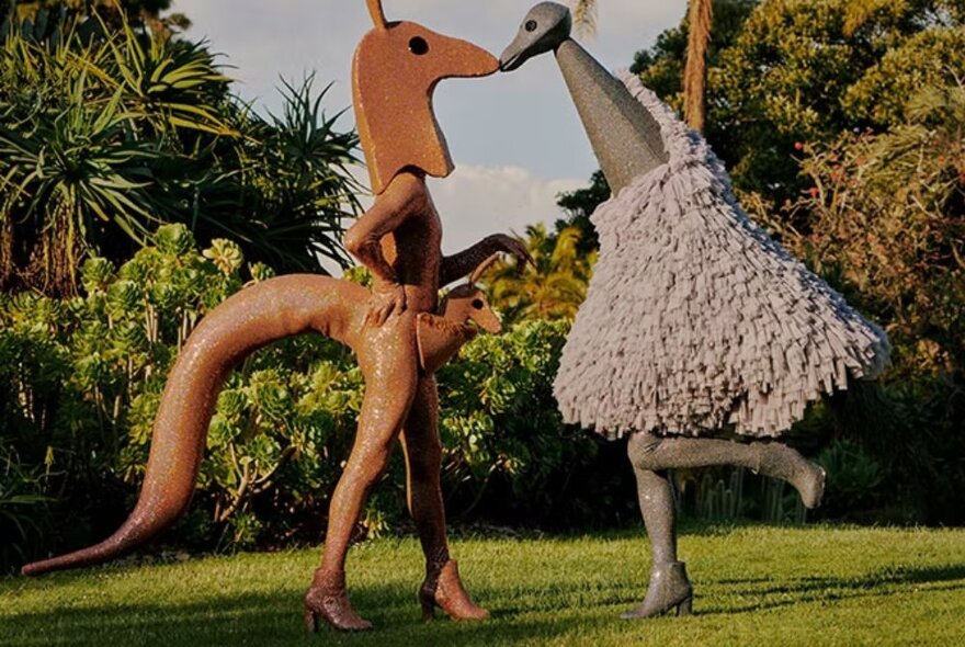 Two people dressed in costumes as Australian animals in a garden setting - a grey emu and a brown kangaroo.