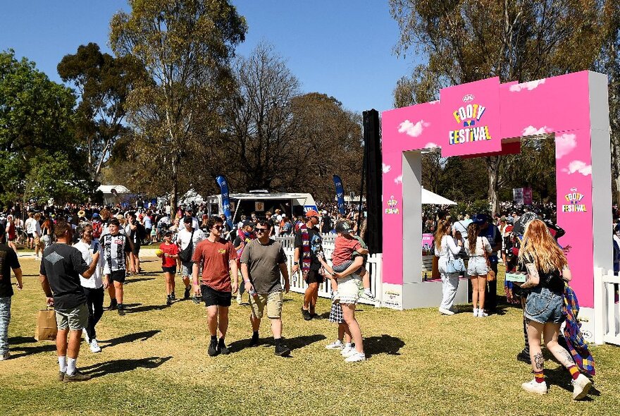 Crowds of people walking around in the sunshine at the AFL Footy Festival in Yarra Park.