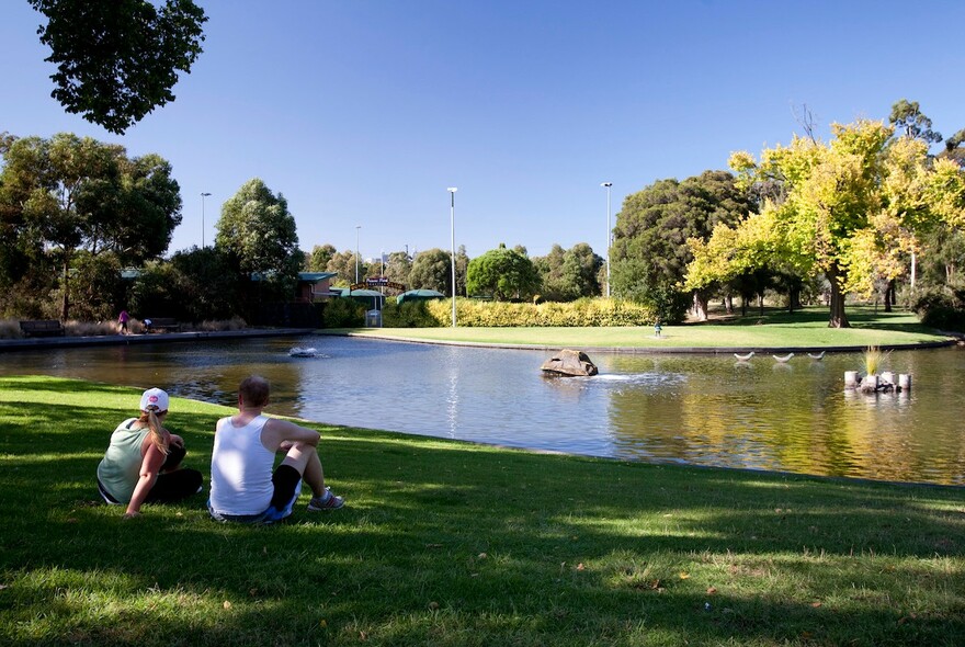 People sitting on the grass by a pond.