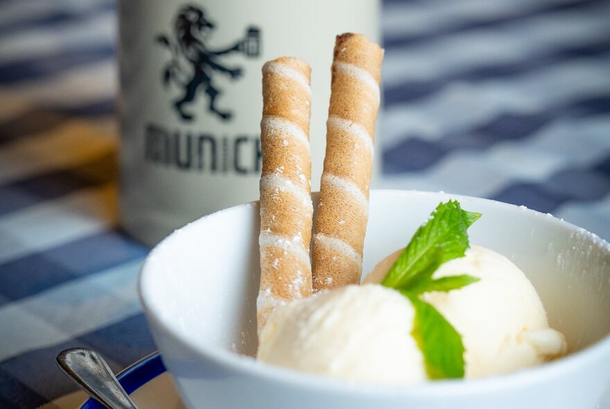 A bowl with two scoops of icecream and sweet biscuits sticks, with a mint garnish.