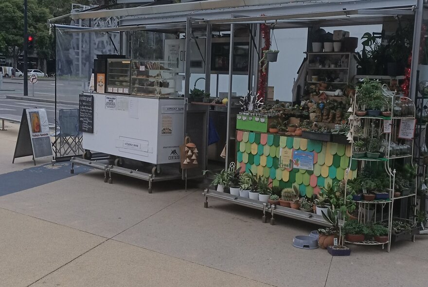 A kiosk in Docklands, selling small plants in pots and food and drinks from a small counter under shelter.