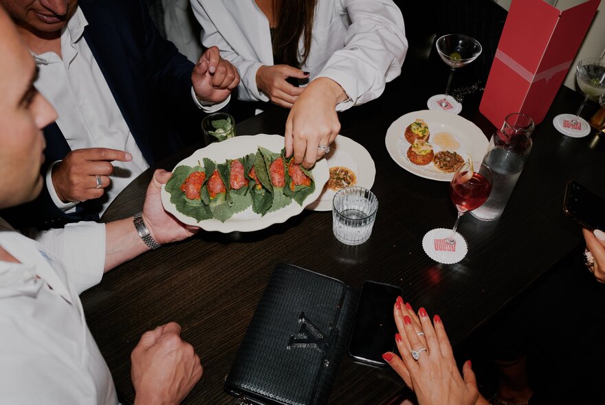 A waiter offers a plate of canapés to a group of people enjoying drinks.