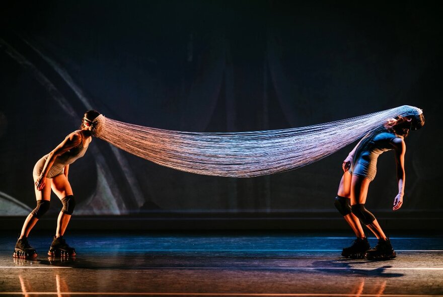 Two members of dance group Neon Dance performing on a darkened stage, their faces joined by many fine threads. 