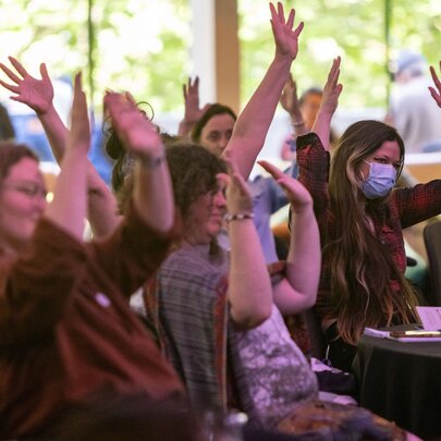 Women in a conference setting, ohlding their arms in the air while seated.