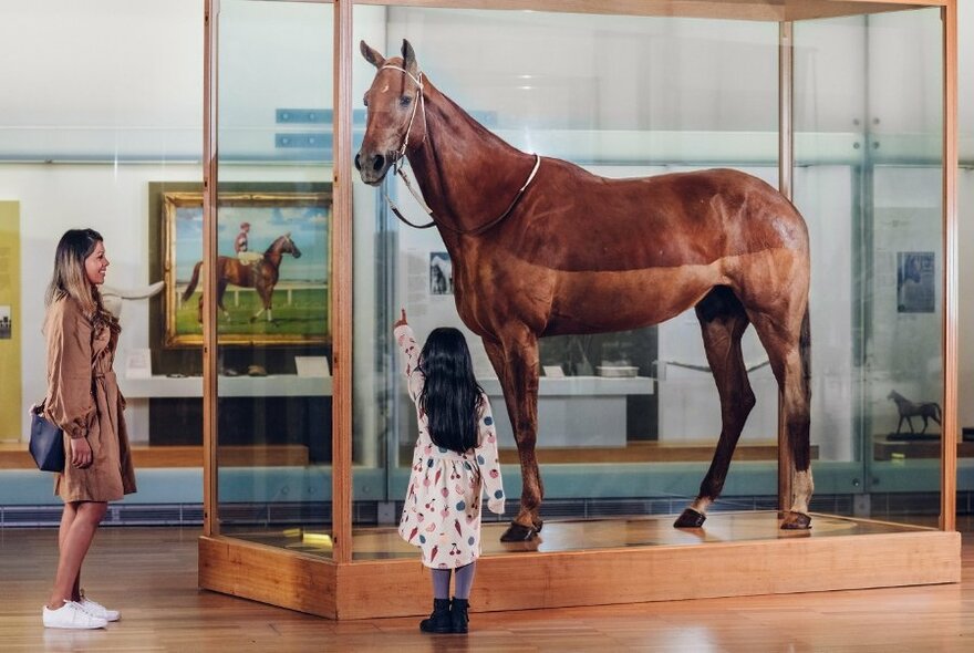 Woman and girl standing looking at the racehorse Pharlap on display inside a glass exhibition case.