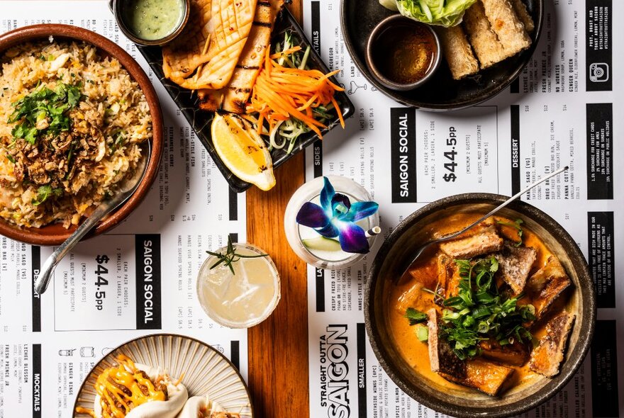 Looking down on assortment of Vietnamese dishes and condiments on a wooden table with menus.