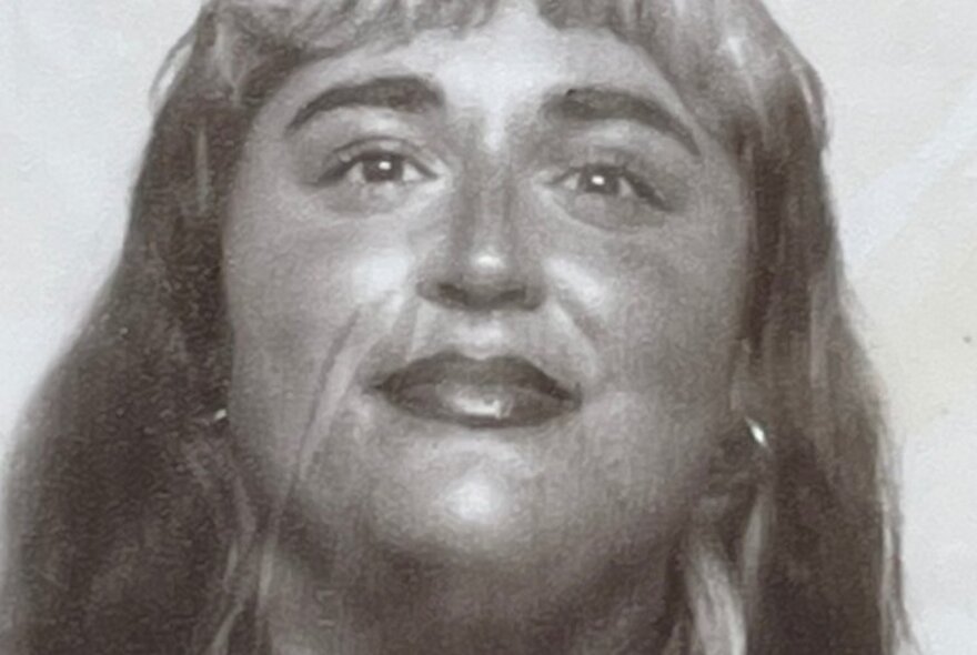 Black and white close up of a face of a young person, with a slight smile, hoop earrings and a fringe.