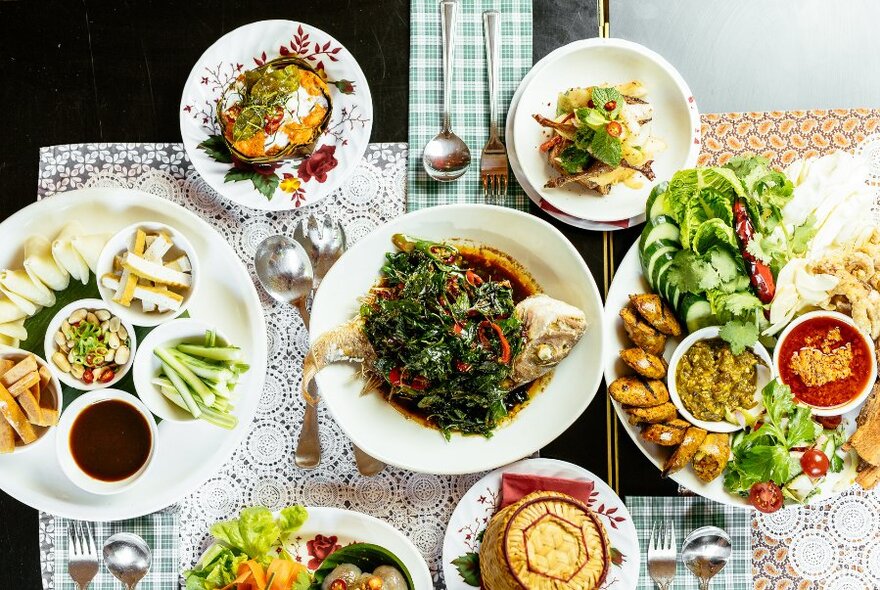 Overhead view of a table with many white plates of food, cutlery and napkins.