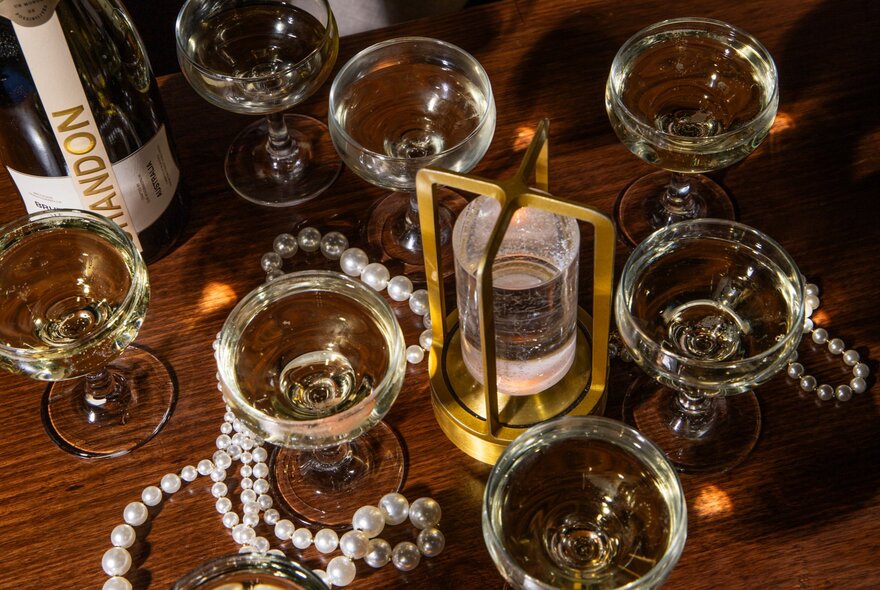 Looking down on a table with many glasses of champagne and pearl necklaces strewn around. 