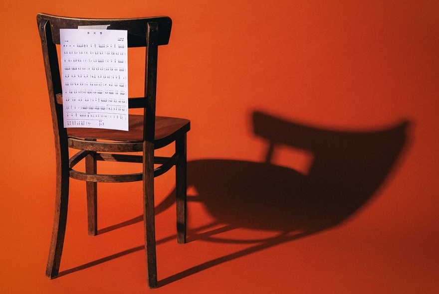 A piece of paper with writing pinned to the back of a wooden chair against an orange background.