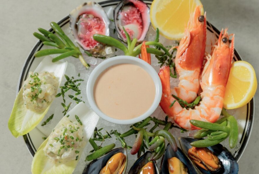 A platter of prawns, mussels and oysters with a dipping sauce.