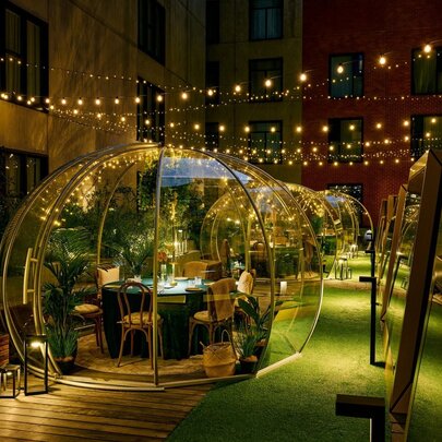 Private dining bubbles in a designed space with greenery and fairy lights.