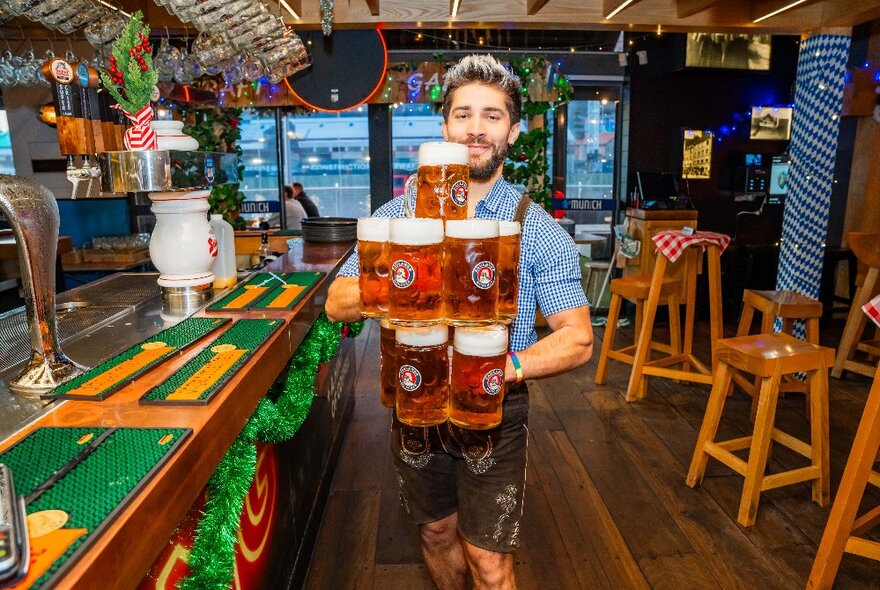 A barman carrying a pile of beer steins in a bar. 