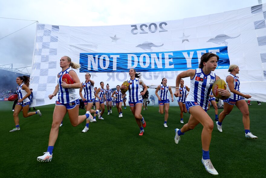 The North Melbourne AFLW team running through the banner before a game.